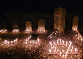 Mehrere Dutzend brennende Kerzen bilden ein leuchtendes Davidstern-Symbol vor Grabsteinen auf dem jüdischen Friedhof in Gardelegen. Aufgenommen beim Pogromgedenken am 9. November 2025.