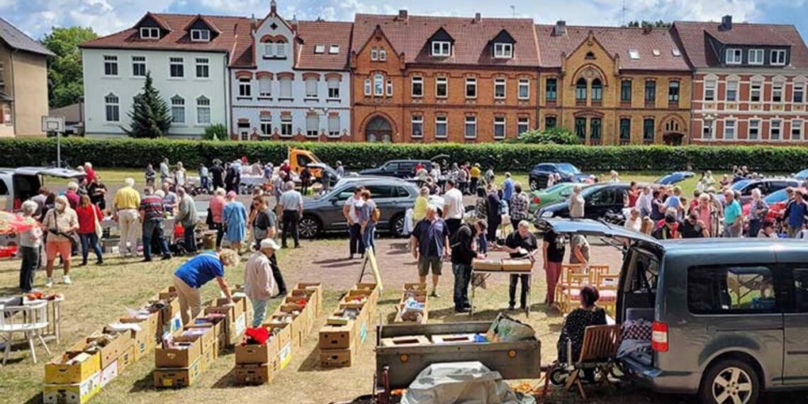 Flohmarkt auf dem Harbig-Sportplatz in Gardelegen: Viele Besucher stöbern bei sommerlichem Wetter an Trödelständen mit Büchern, Kleidung und Gebrauchtwaren – im Hintergrund die Gründerzeitfassaden der Schillerstraße.