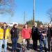 Gruppe von Menschen steht neben einem neu aufgestellten Storchenmast mit Nisthilfe in Roxförde bei Gardelegen. Das Detail-Bild links zeigt die Mastspitze mit der Storchen-Nisthilfe vor blauem Himmel.