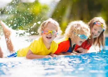 Kinder und Jugendliche spielen und schwimmen bei sommerlichem Wetter in einem Freibad der Hansestadt Gardelegen zum kostenlosen Kindertagseintritt.