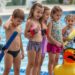 KI-generiertes Symbolbild: Kinder lernen in einem Freibad schwimmen und stehen mit Schwimmhilfen am Beckenrand. Die Hansestadt Gardelegen plant 2026 mehrere Schwimmkurse für Kinder in den Freibädern Zienau, Potzehne und Zichtau.