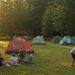 KI-generiertes Symbolbild eines Sommercamps mit bunten Zelten und Jugendlichen auf einer grünen Wiese.